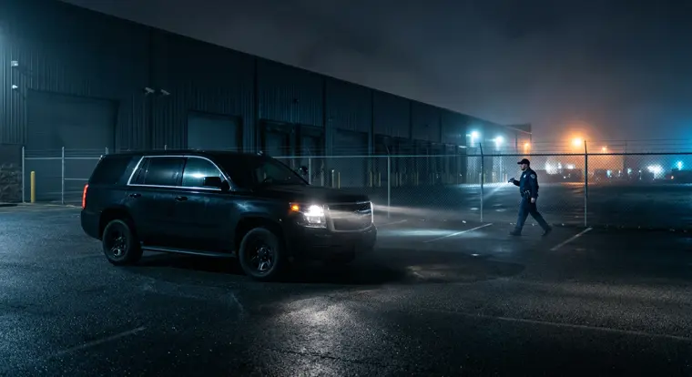 Security patrol vehicle and an officer checking a warehouse perimeter after dark